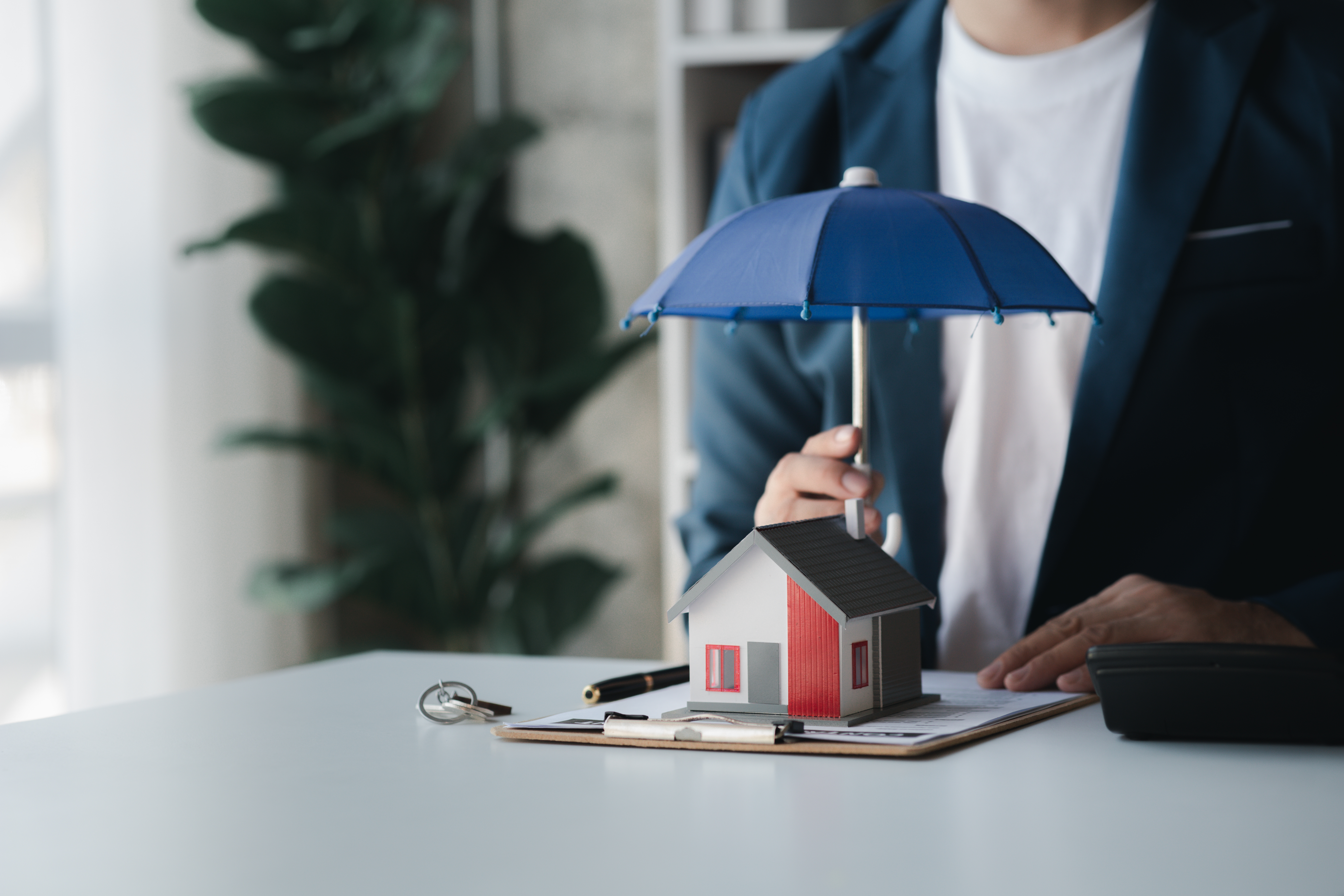 An umbrella is held over a model home, representing the protection insurance agencies provide.