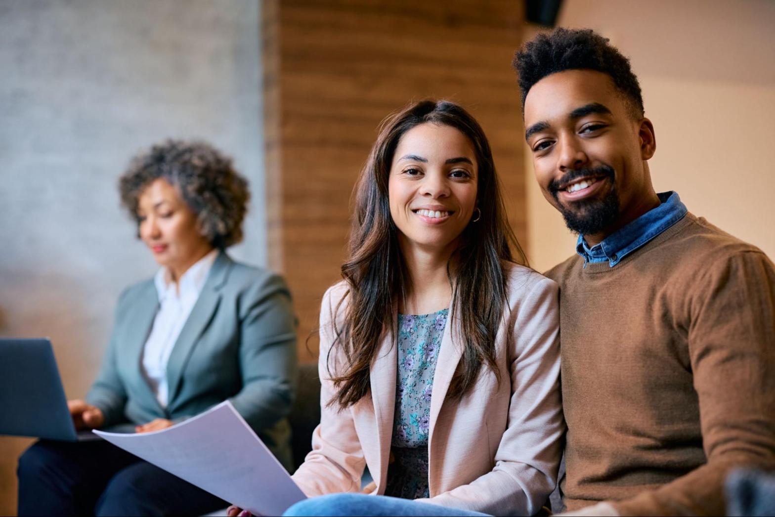 A couple are sitting together holding paperwork in an office.