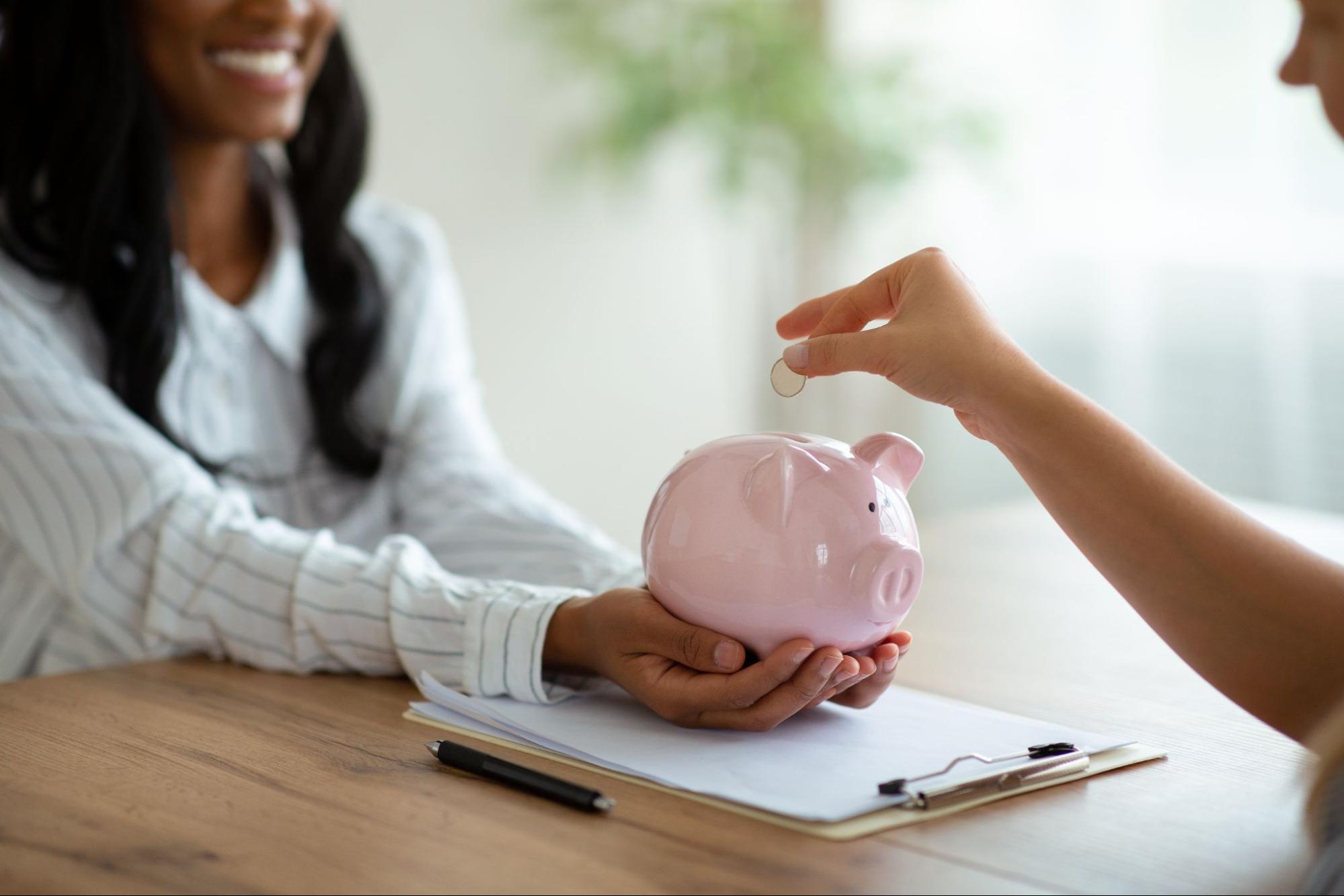 Dropping a coin into a piggy bank held by a woman to symbolize financial planning.