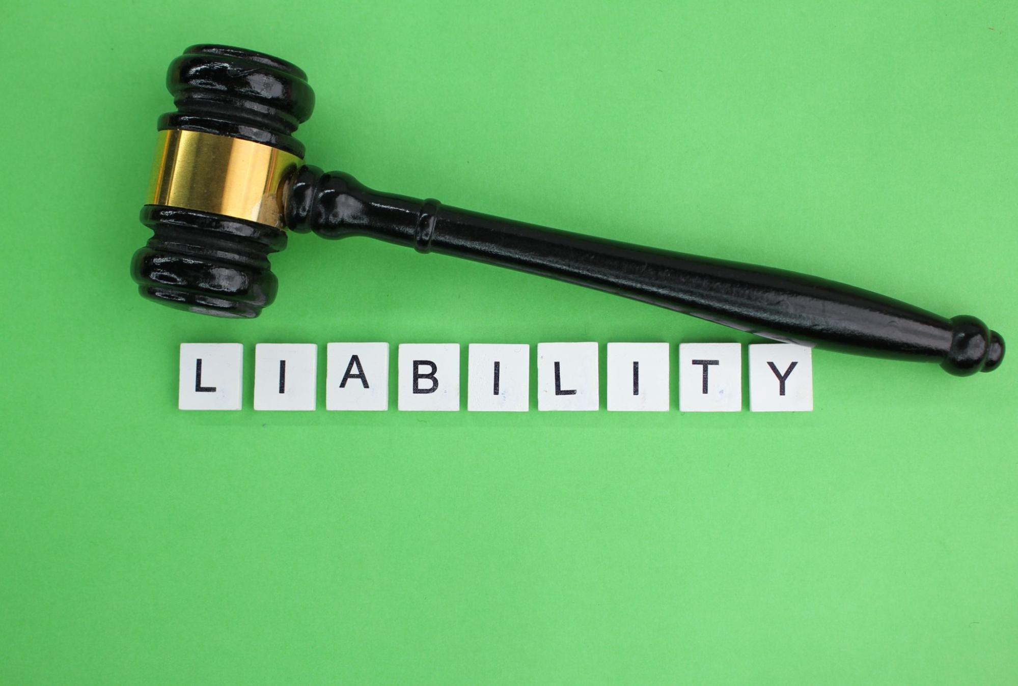 A black gavel placed on liability letter blocks on a green surface
