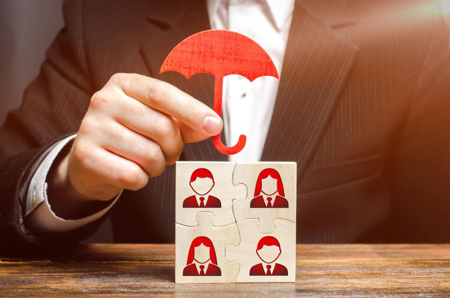 Closeup on a hand holding a small umbrella over images of employees.