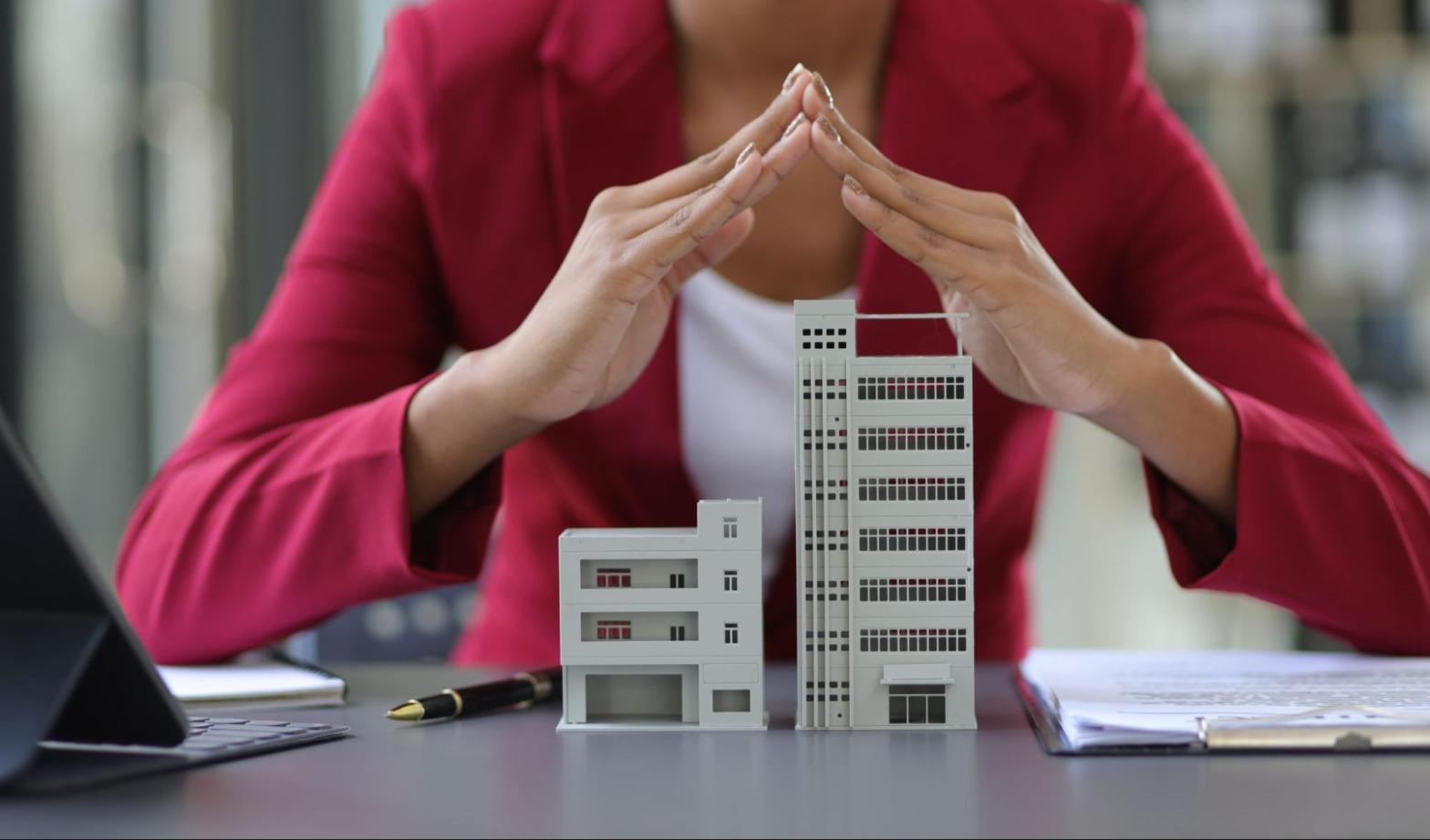 Cropped view of a female executive in a red suit shielding buildings with her hands