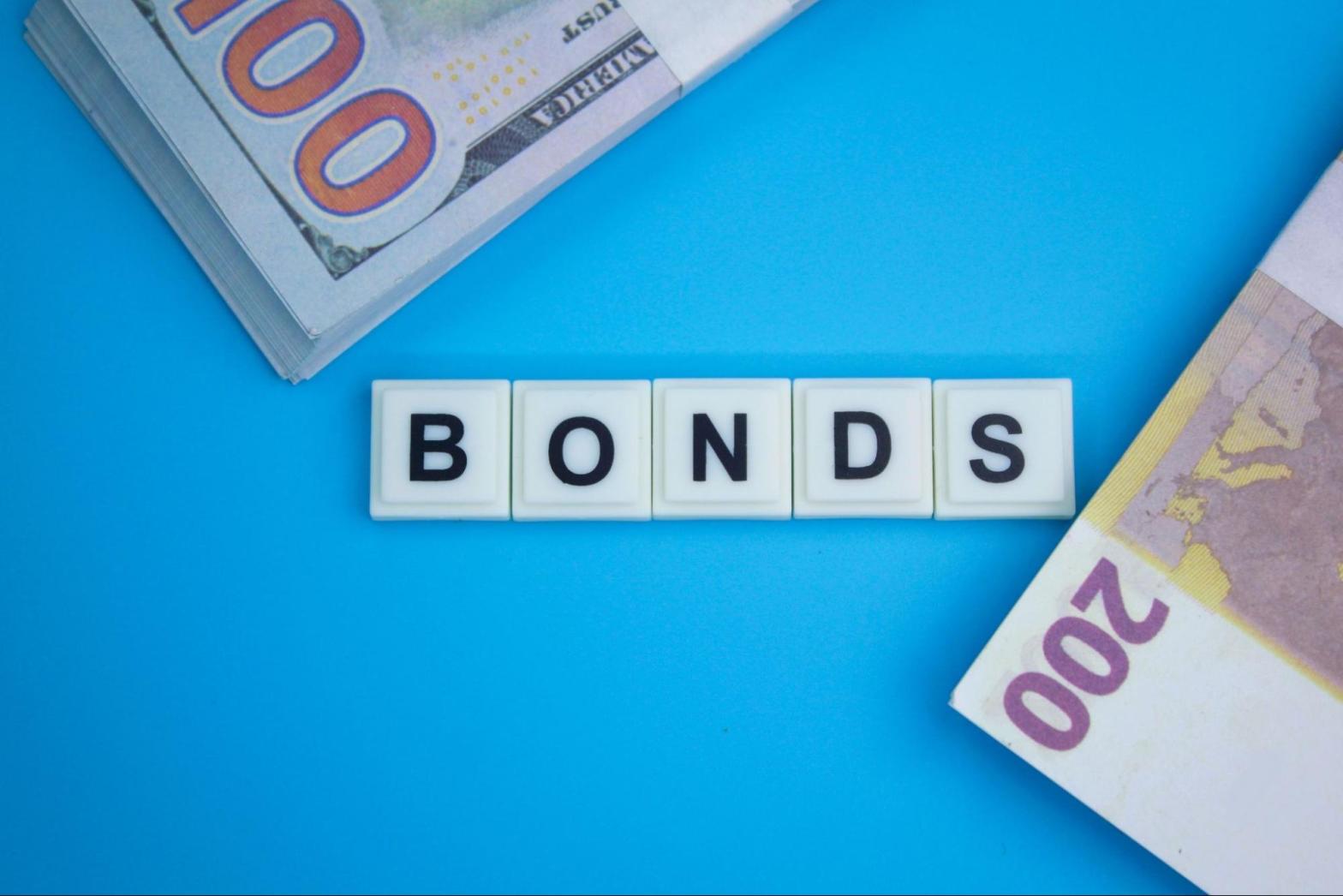 Scrabble tiles spelling “bonds” beside euro and dollar currency symbols on a blue surface