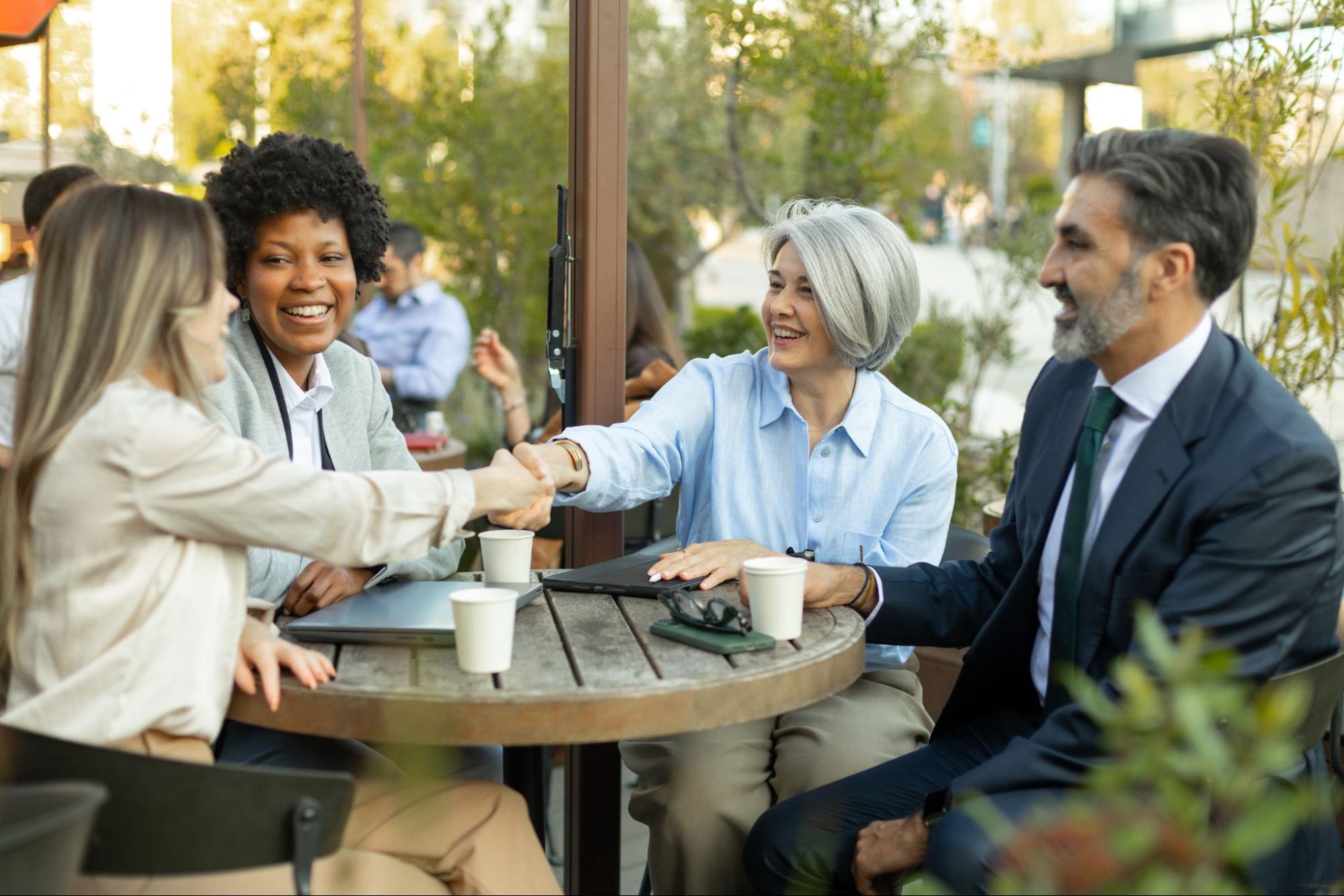 Insurance advisor and business owner shaking hands after reviewing coverage options at an outdoor café with colleagues