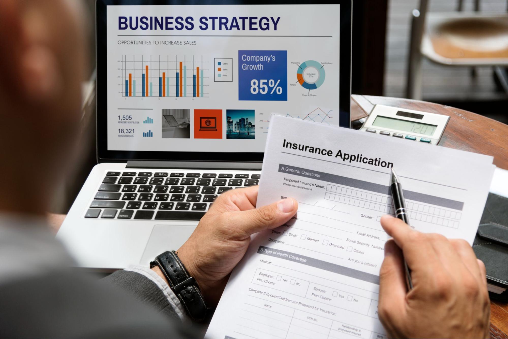 Businessman reviewing an insurance application form while analyzing a business strategy plan on his laptop