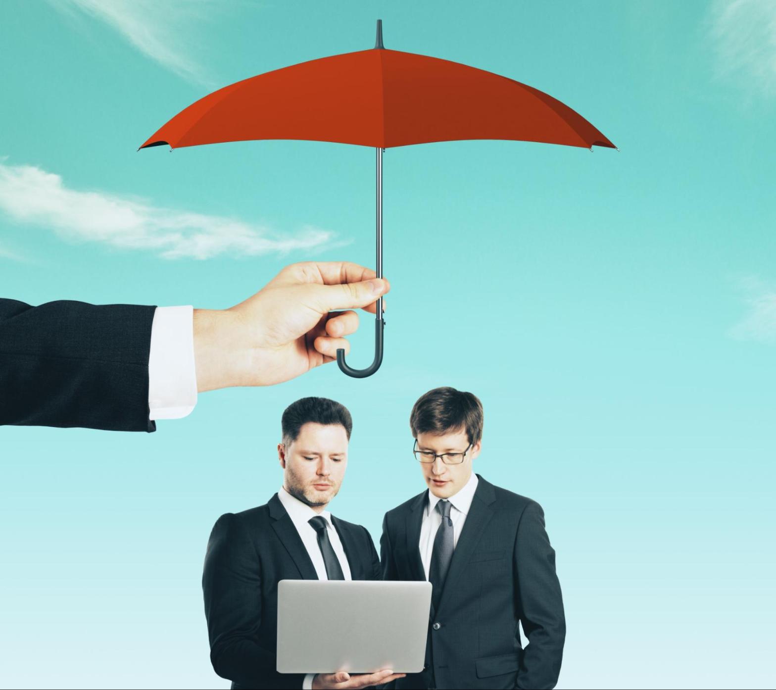 Businessmen working on a laptop under a red umbrella held overhead, representing business protection and risk coverage