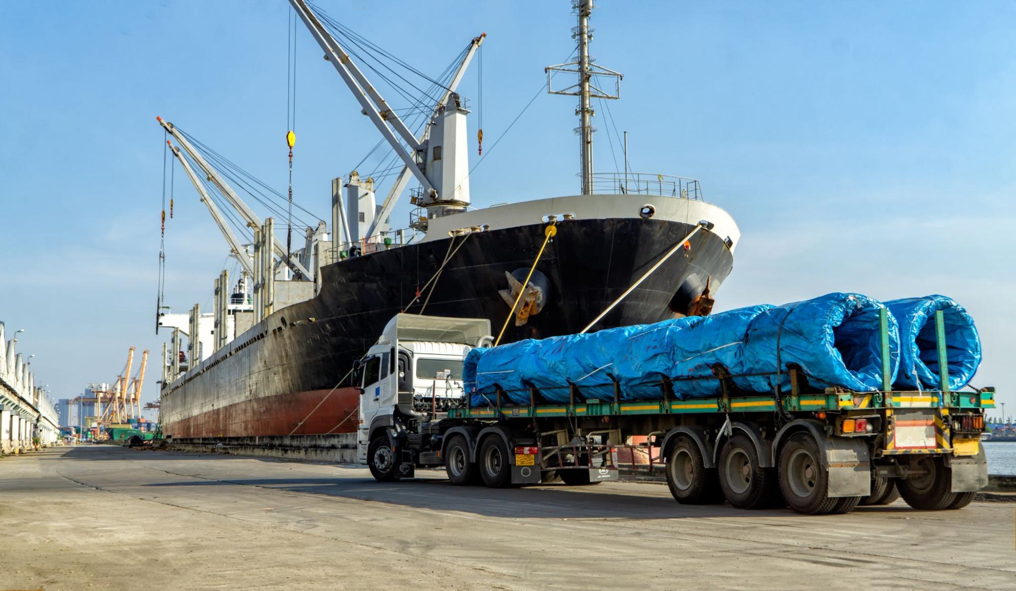 Cargo ship and truck transporting blue coiled material, representing inland marine insurance coverage for goods in transit