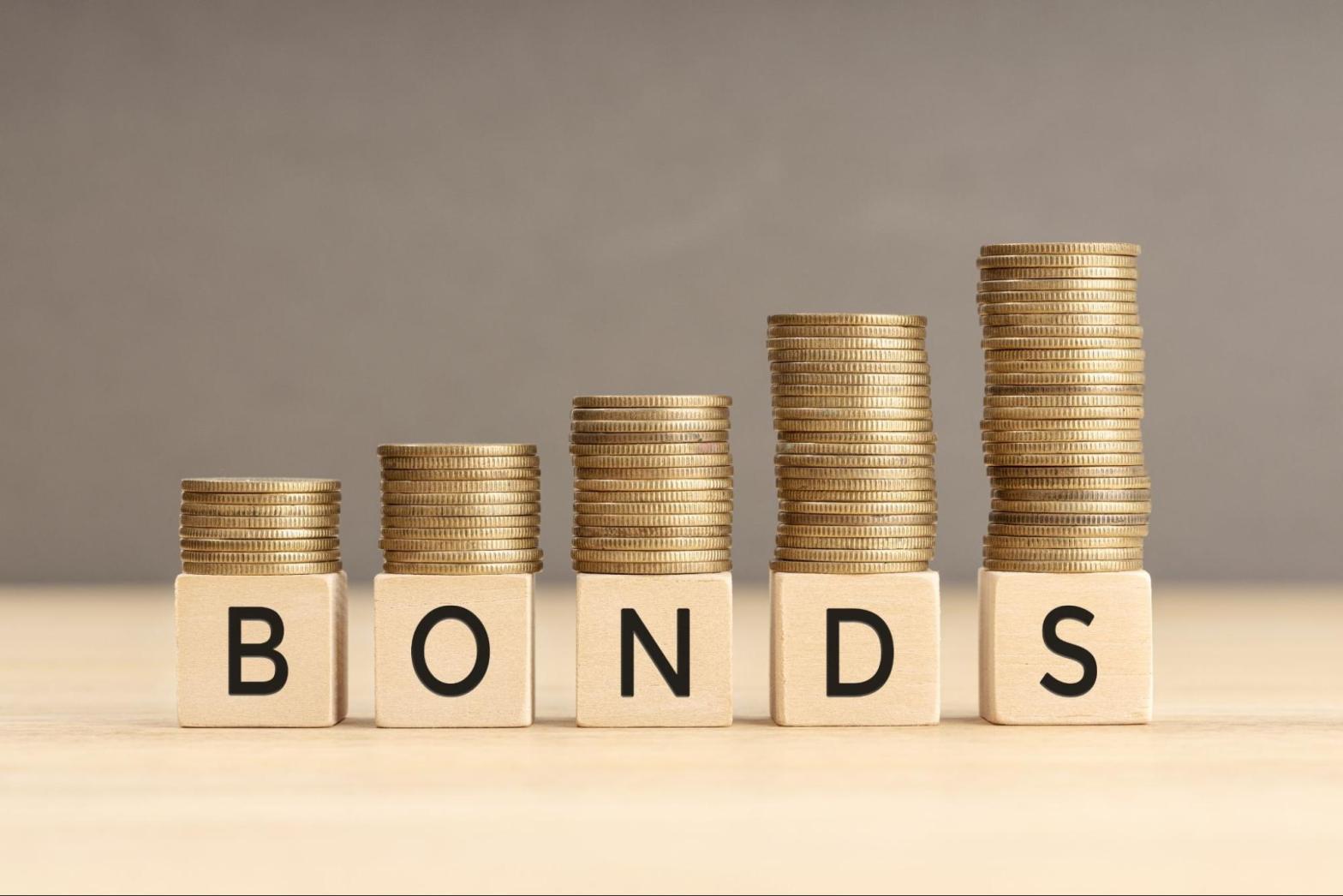 Ascending coin stacks behind wooden blocks spelling "BONDS" representing surety bond rates and financial security