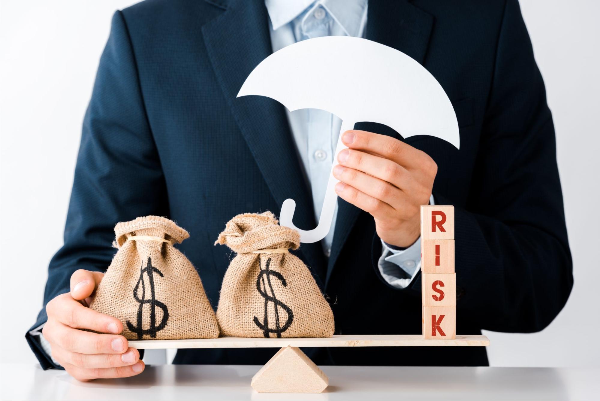 Businessman holding a protective umbrella over money bags and legal scales, representing excess liability coverage, risk management, and asset protection