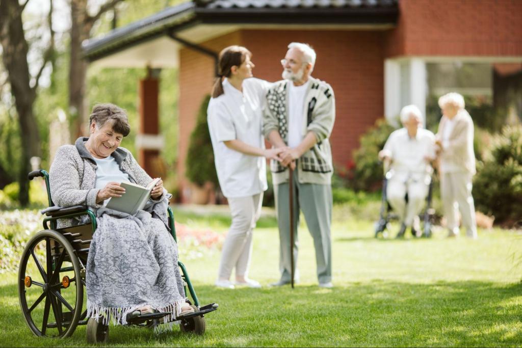 Senior woman reading in a senior living facility garden while other residents engage in activities with caregivers